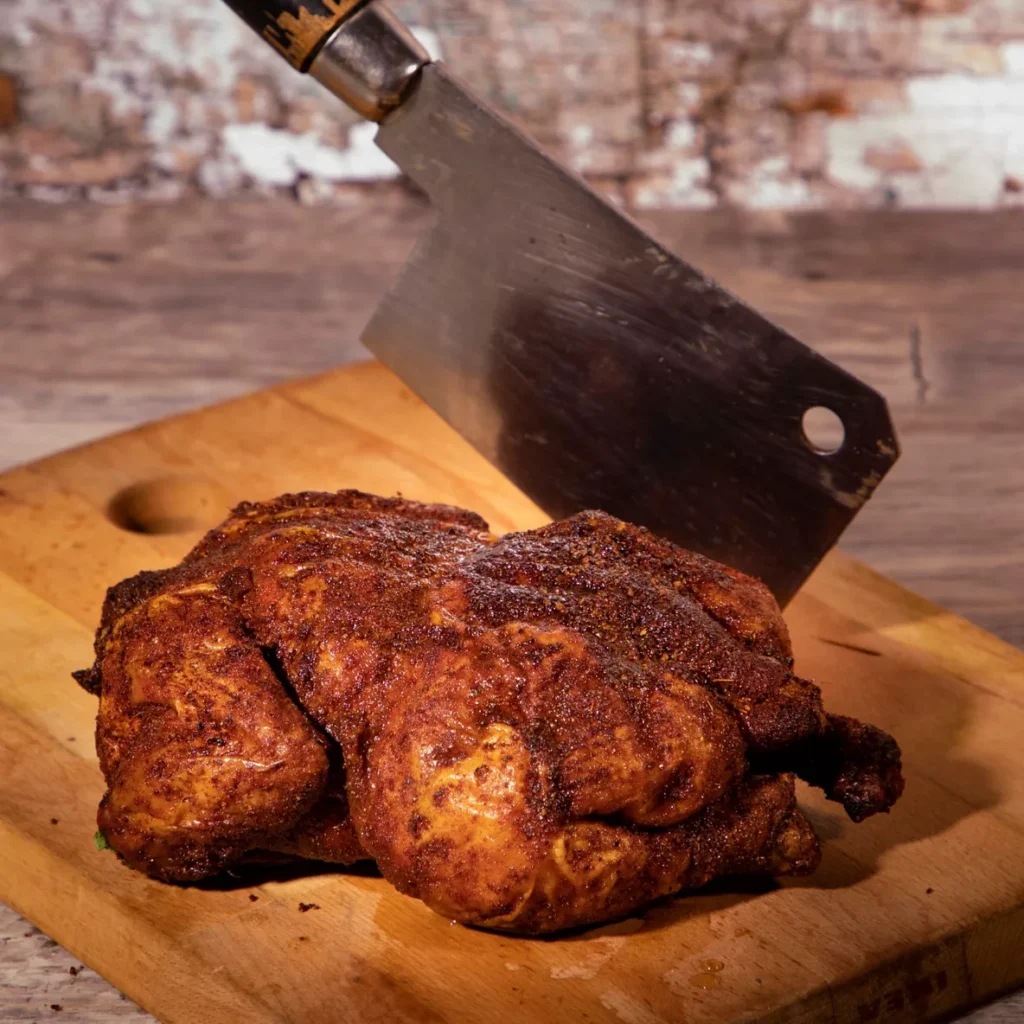 Juicy roasted chicken on wooden board with cleaver.