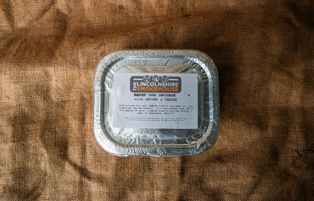 Aluminum foil container with a food label on a brown fabric background.