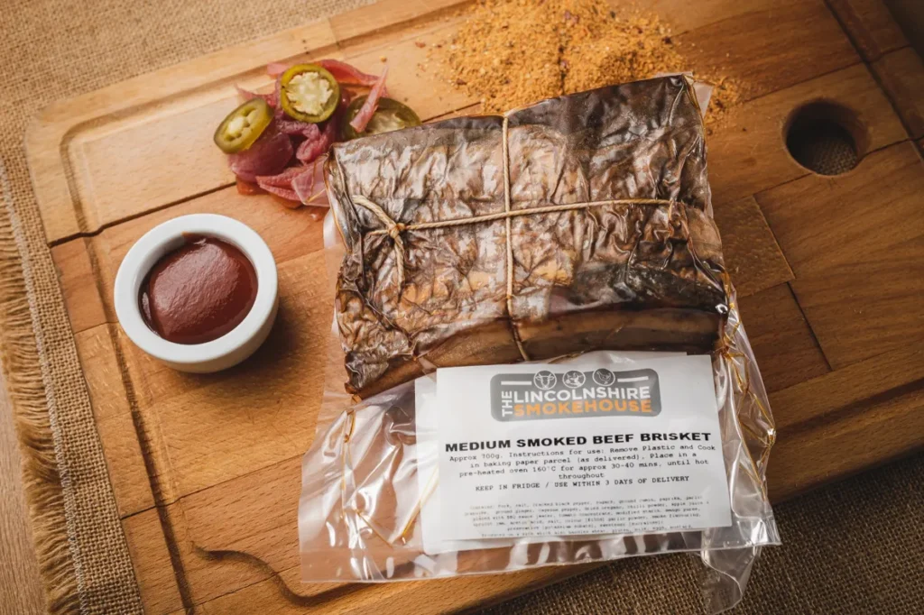 Smoked brisket wrapped in butcher paper on a wooden board with sauce and sides.